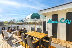 A rooftop deck with outdoor furniture, a wooden table, and two green umbrellas. The name "Music City" is visible on the building. - Bluegrass Bungalow 2 | Parkside Views | Nashville Vibes (Nashville)