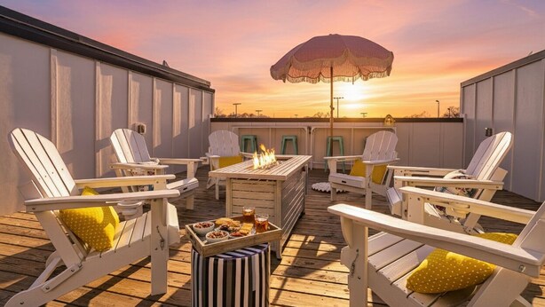 A rooftop deck with white Adirondack chairs, a fire pit, and a table with food and drinks.