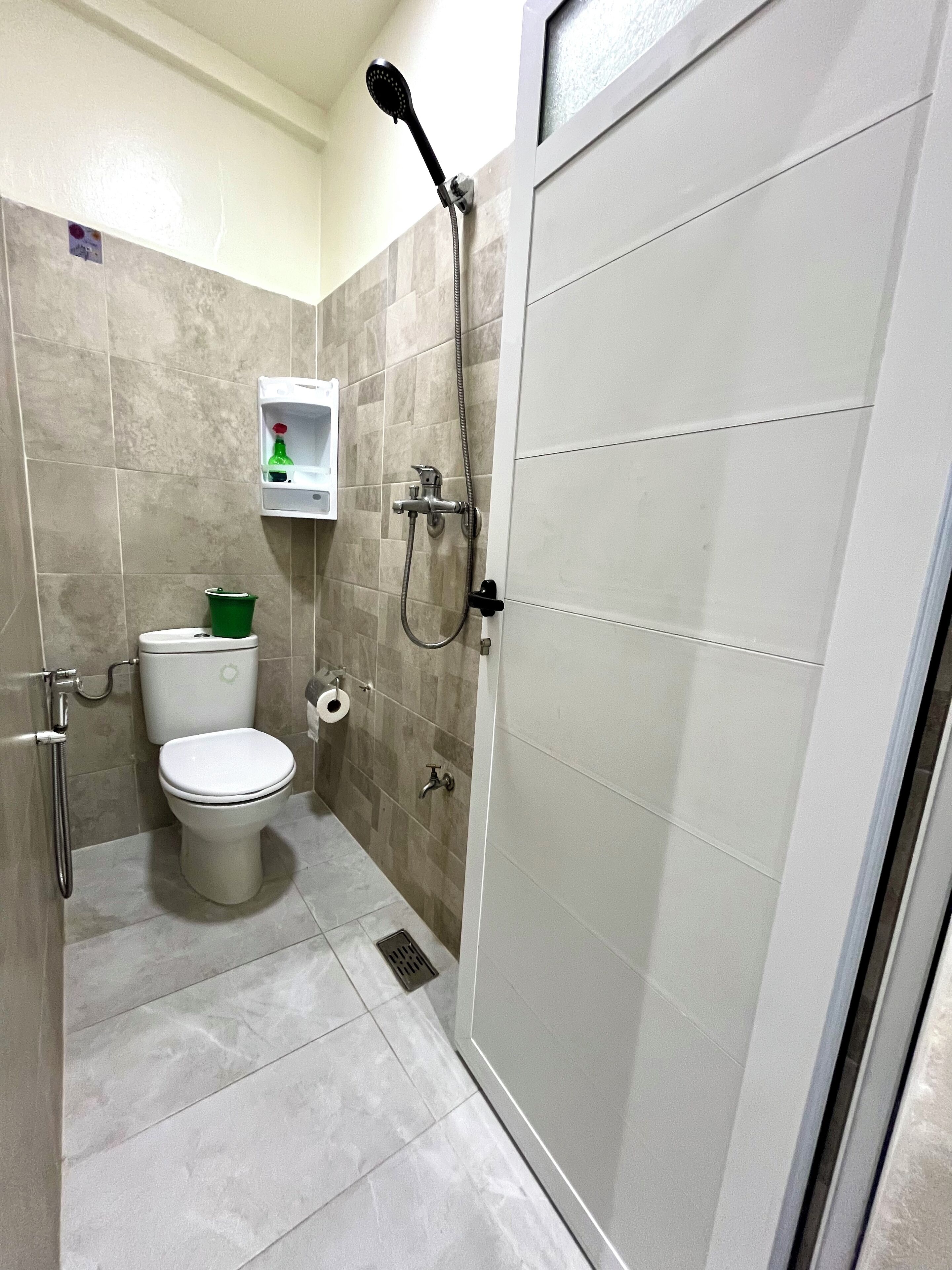 Een badkamer met toilet, douche en een klein plankje met toiletartikelen.