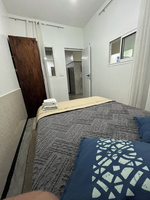 A bedroom with a bed, a wooden door, a window, and a bathroom visible through an open door. - Maison Calme à Proximité de la mer (Agadir)