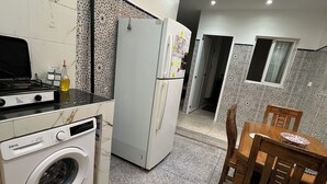 A compact kitchen with a washing machine, a refrigerator, a dining table with chairs, and a tiled backsplash. - Maison Calme à Proximité de la mer (Agadir)