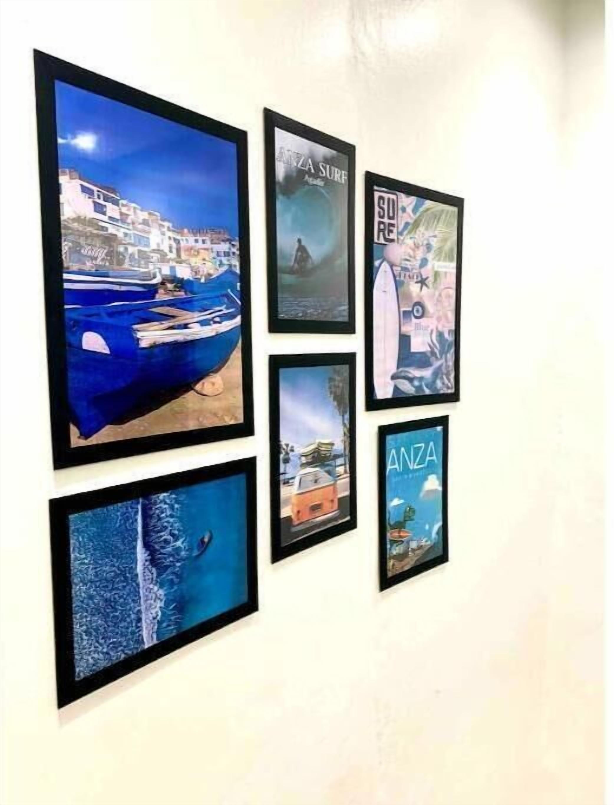 Un mur orné de six tableaux encadrés représentant des paysages côtiers, notamment des bateaux et des bâtiments.