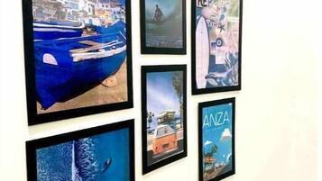 Un mur orné de six tableaux encadrés représentant des paysages côtiers, notamment des bateaux et des bâtiments.