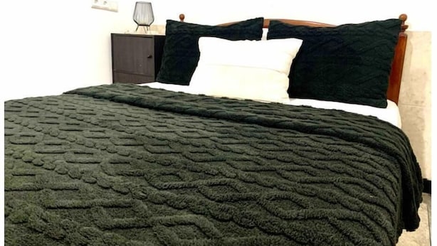 A bed with a dark green textured blanket, a white pillow, and a dark green pillow on a wooden headboard. - Maison Calme à Proximité de la mer (Agadir)