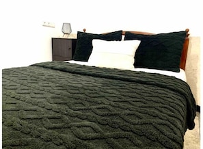 A bed with a dark green textured blanket, a white pillow, and a dark green pillow on a wooden headboard. - Maison Calme à Proximité de la mer (Agadir)