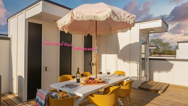 A dining area with a table set for two, yellow chairs, a striped umbrella, and a bottle of wine.