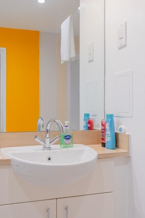 Une salle de bain avec un lavabo blanc, un miroir et des articles de toilette posés sur le comptoir.