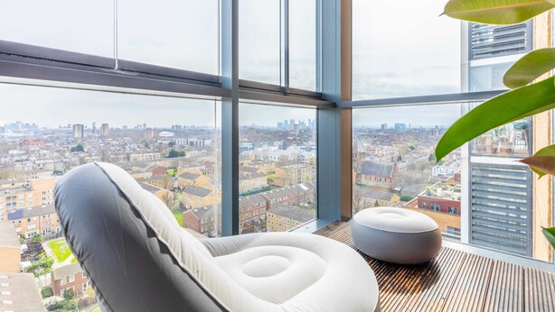Ein modernes Zimmer mit einem großen Fenster, einem weißen gepolsterten Sessel und einem kleinen Ottomanen.