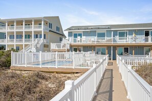 A beachfront hotel with multiple balconies, a pool, and a wooden boardwalk.