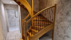 A wooden spiral staircase with a metal railing, leading to an upper floor. The walls are textured, and the floor is tiled.