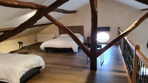 An attic bedroom with exposed wooden beams, two beds, a small table, and a window.