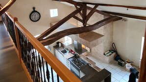 A kitchen with a wooden ceiling beam structure, a clock on the wall, and a window providing natural light.