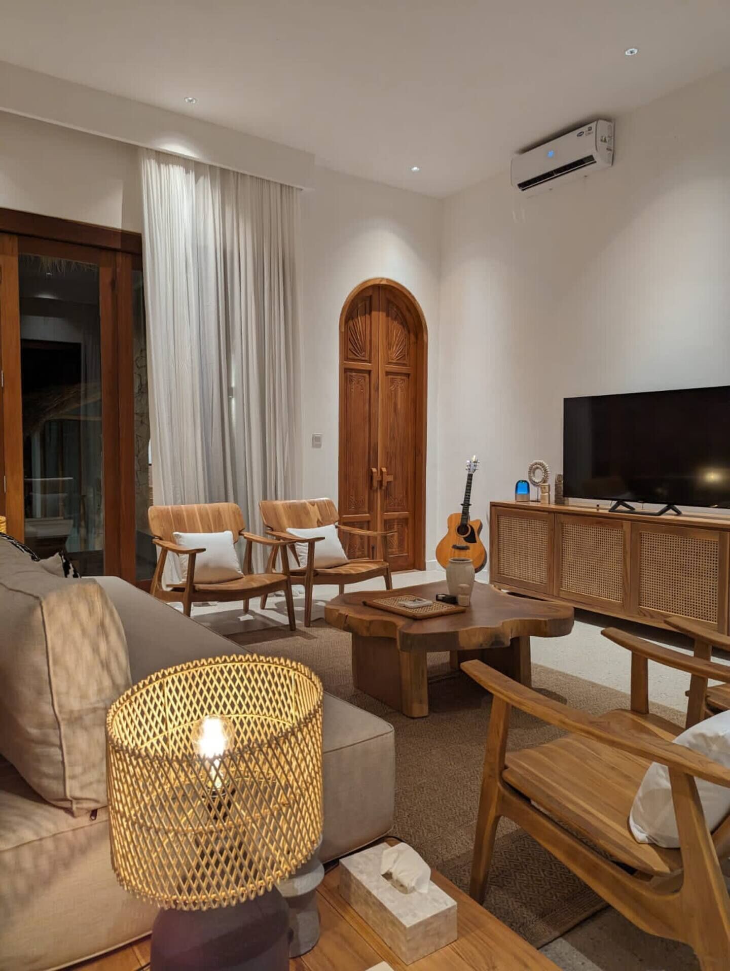 Uma sala de estar moderna com um sofá, cadeiras de madeira, uma mesa de centro, uma televisão e uma guitarra.