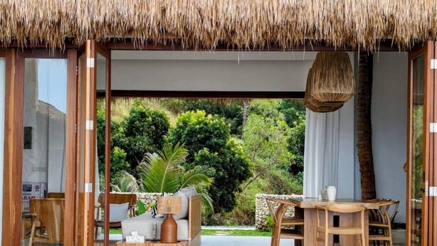 Uma área externa moderna com piscina, móveis de madeira e telhado de palha.