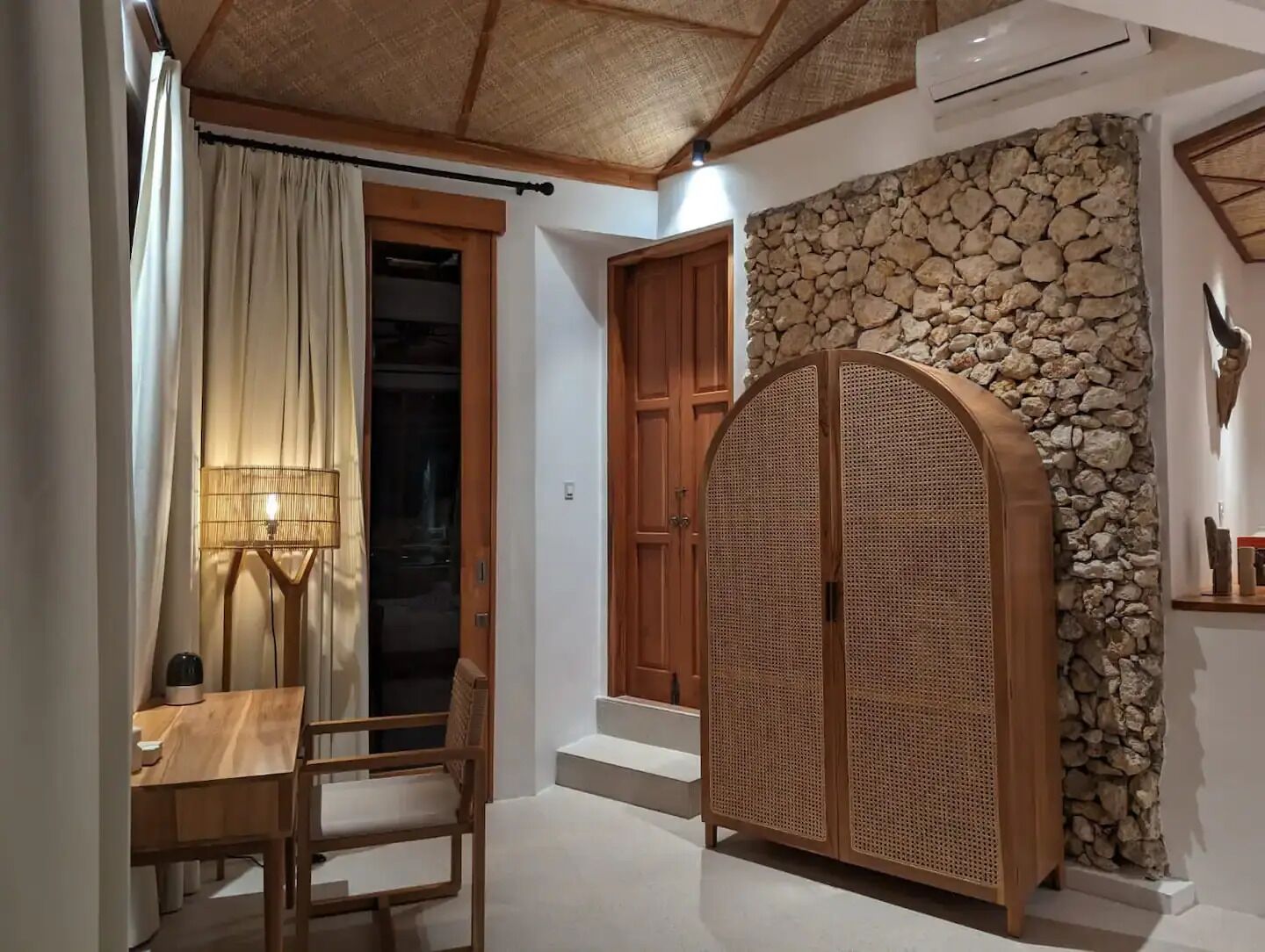 Quarto com mesa de jantar, cadeiras, luminária, guarda-roupa de madeira e parede de pedra.