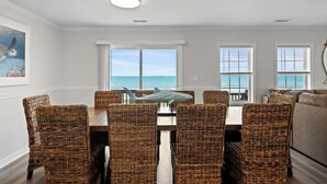 Un coin repas avec des chaises en osier, une table et une vue sur l’océan grâce à de grandes fenêtres.