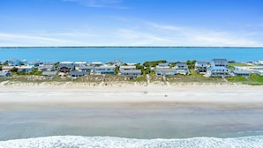 Un quartier résidentiel situé sur la côte, avec des propriétés donnant sur la plage, un ciel dégagé et une vue sur l’océan.
