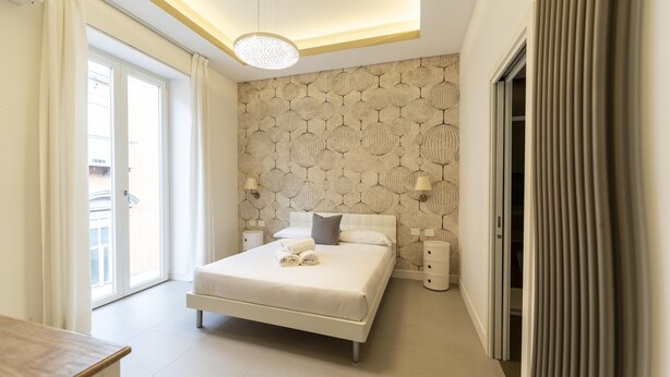 A modern bedroom with a large bed, a ceiling light fixture, and a patterned wall. - Via Concezione a Montecalvario 19 - Camera 3 (Naples)