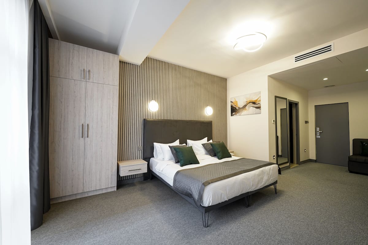 A modern hotel room with a large bed, a wardrobe, a bedside table, and a wall-mounted artwork.