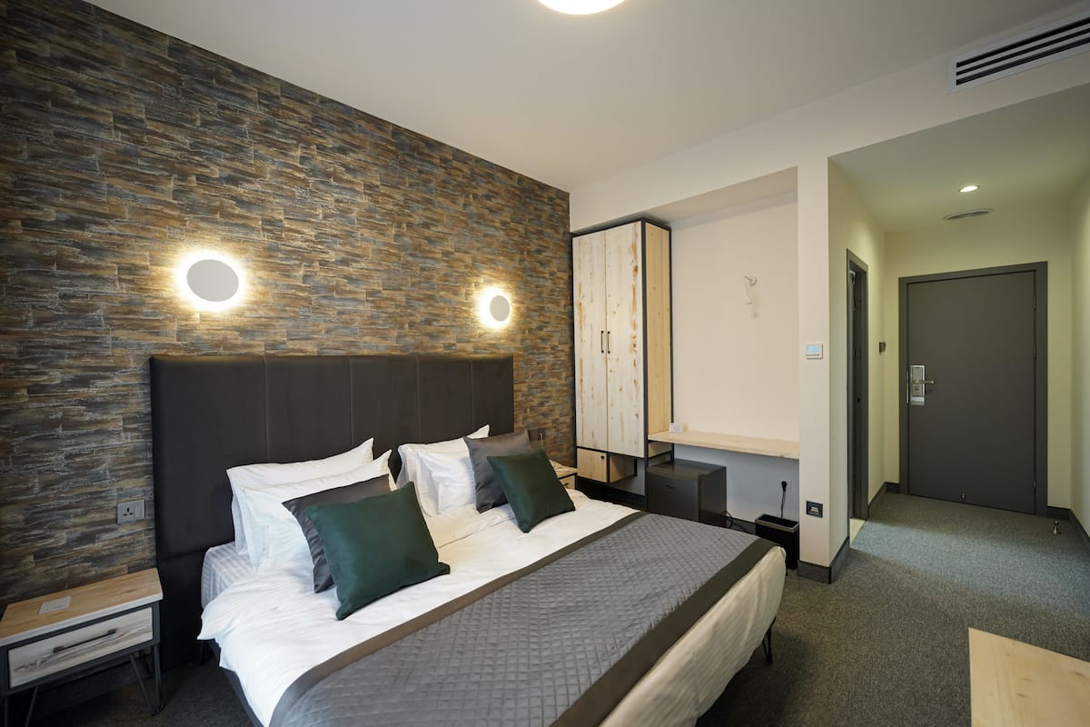 A modern hotel room with a large bed, a stone accent wall, and a wardrobe.