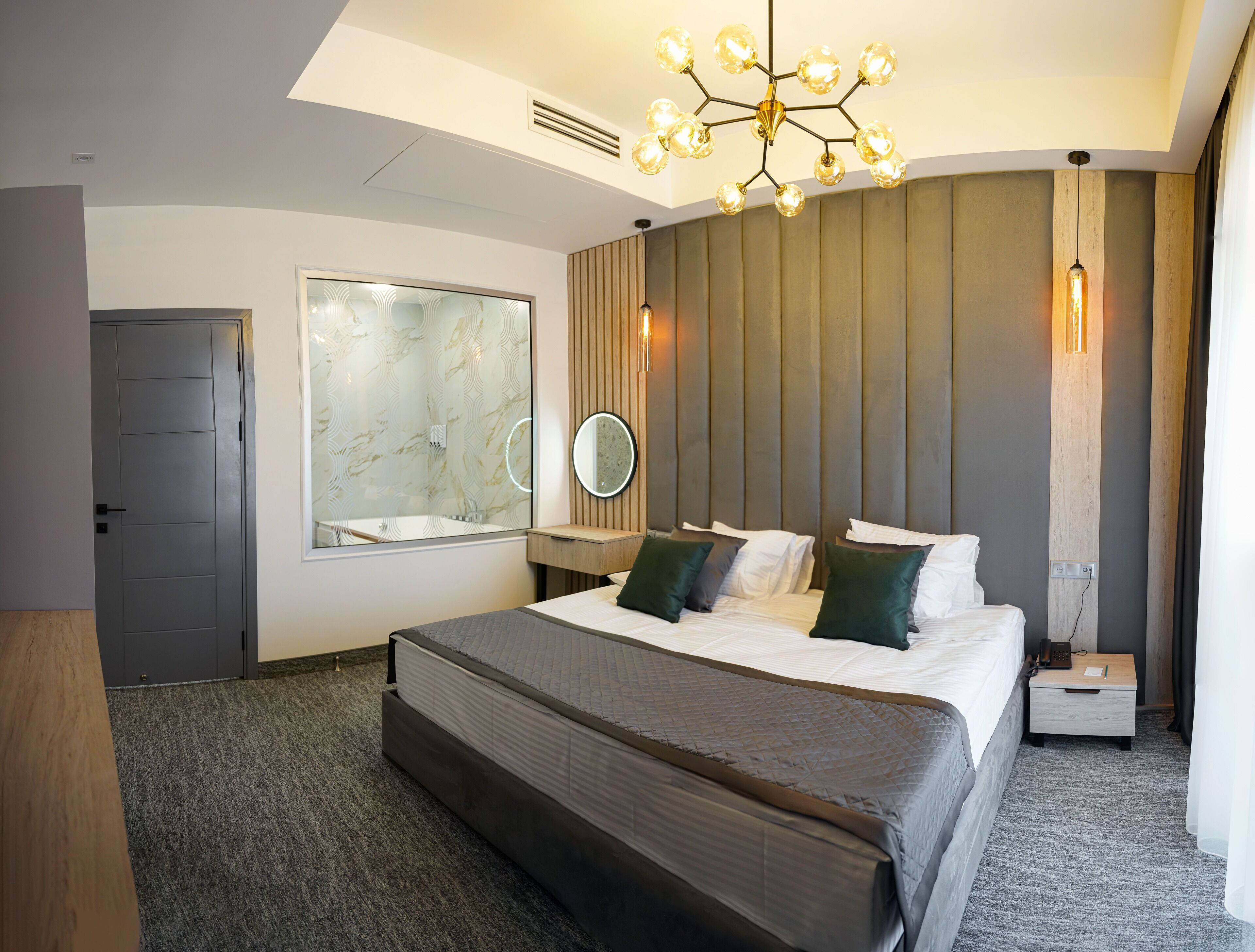 A modern hotel room with a large bed, a mirror, a bedside table, and a unique chandelier.