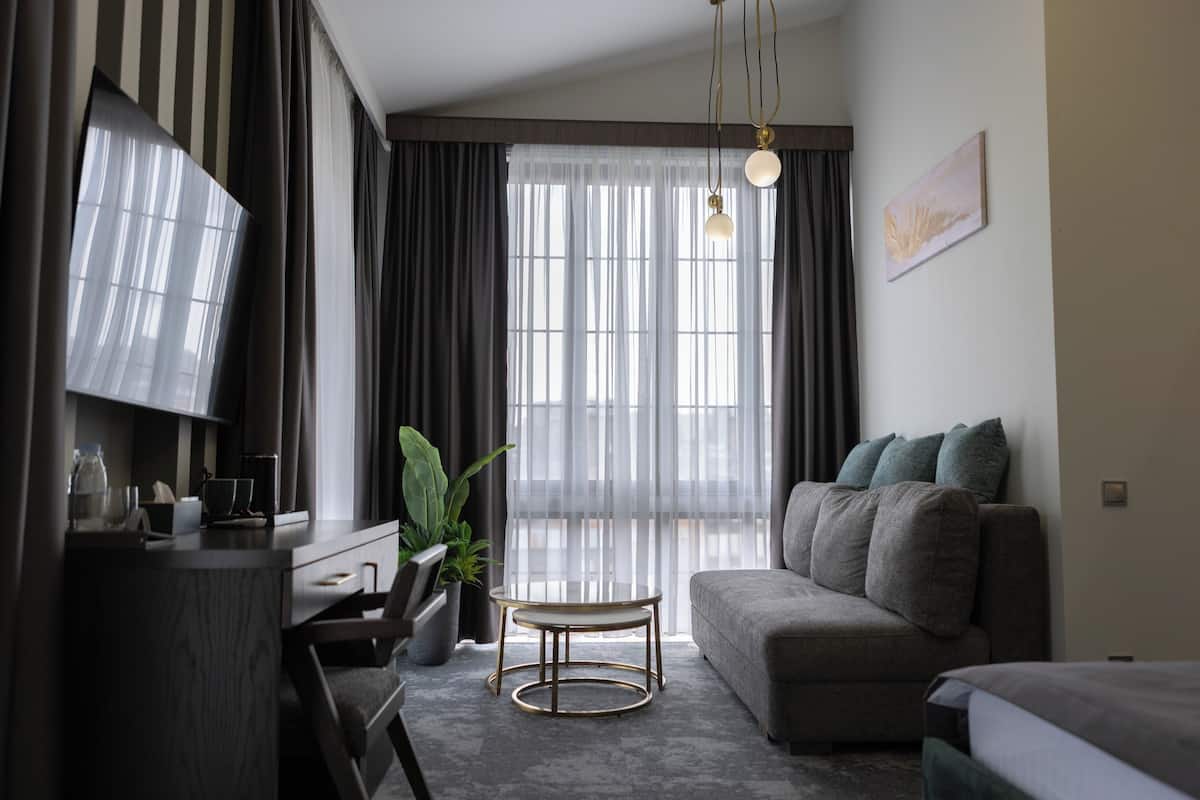 A modern living room with a sofa, a TV, a round coffee table, and a large window with curtains.