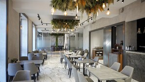 Un restaurant modern amb sòcols de marbre, cadires tapissades de gris i plantes penjants amb llums a la vista.