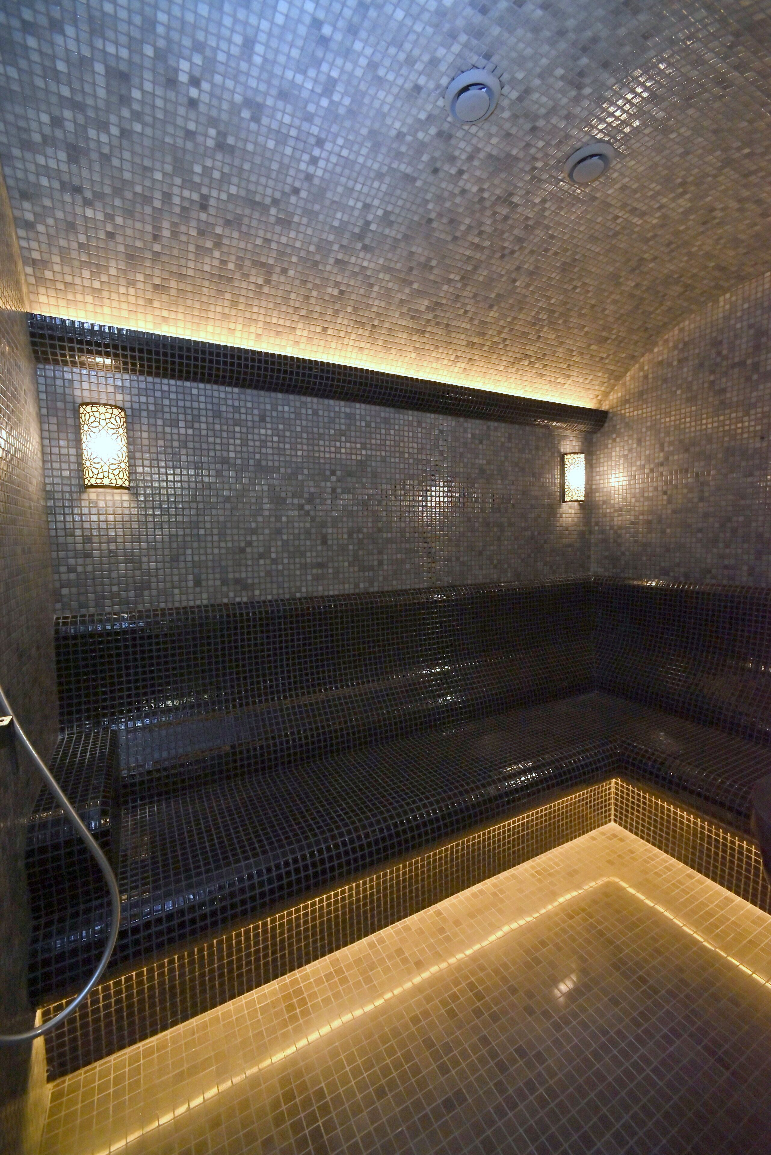 A tiled room with a bench along one wall and a small window with a light fixture.
