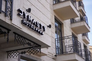 Een hotelschild met de naam 'SYNASTY HOTEL' en decoratieve metalen versieringen.