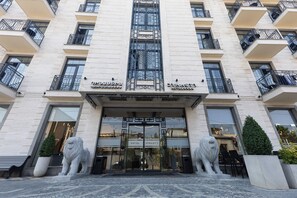 A hotel entrance with two lion statues, a large glass door, and balconies with black railings. - Dynasty (Yerevan)