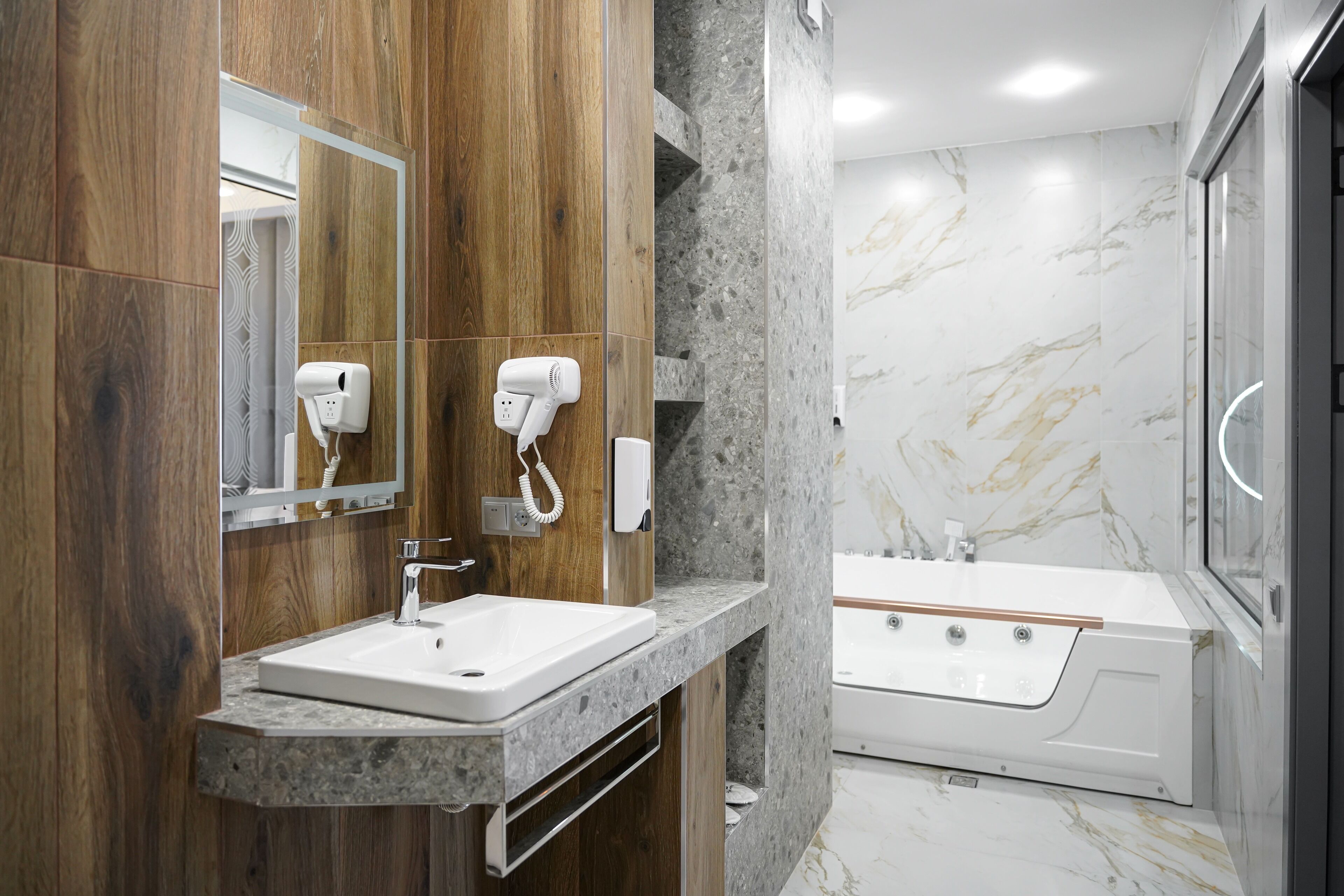 A modern bathroom with a wooden vanity, a marble sink, and a freestanding bathtub.