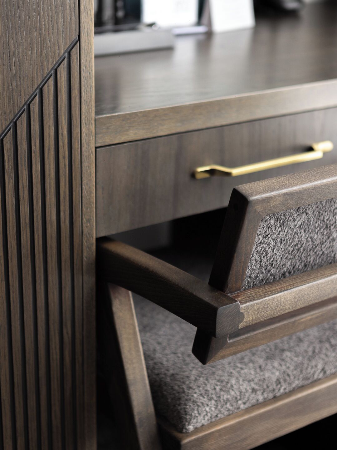 Un bureau en bois avec un tiroir, une poignée dorée et une étagère grise à la texture particulière.