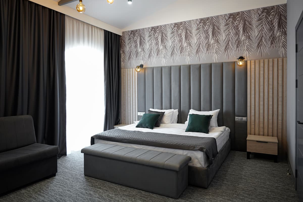 A modern hotel room with a large bed, a sofa, a bench, and a nightstand.