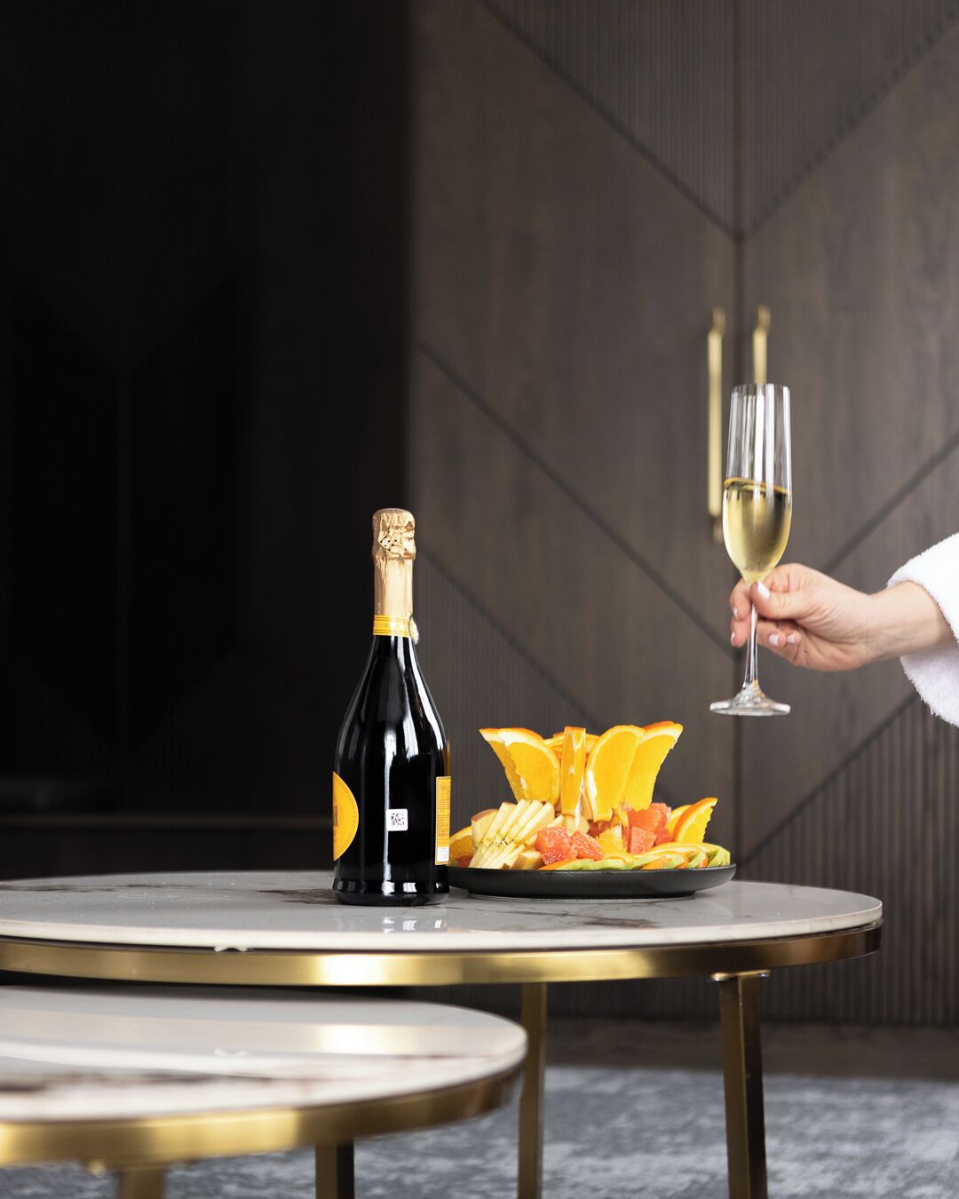 Een fles champagne, een wijnglas en een schaal fruit op een ronde tafel.