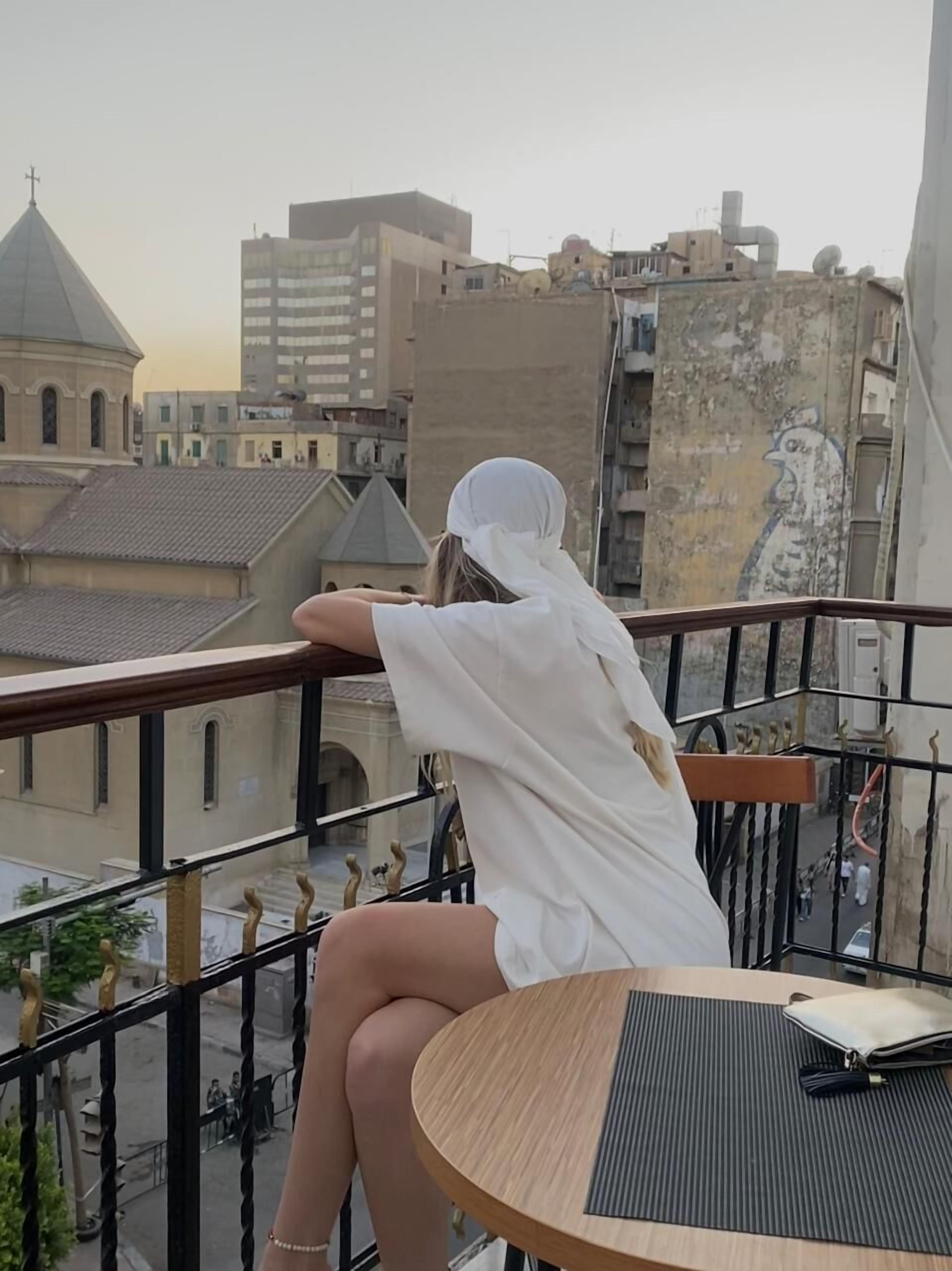 A person sitting on a balcony with a view of buildings and a mural.