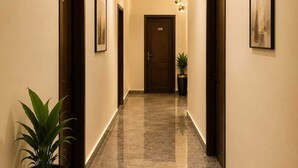Un pasillo con piso de mármol pulido, puertas de madera oscura y una planta en maceta.