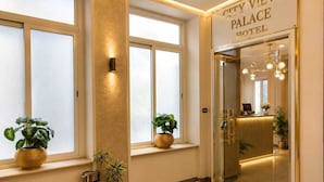 Entrada de hotel con un letrero que dice 'CITY VIEW PALACE HOTEL', ventanas amplias y plantas en macetas.