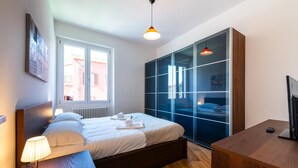 A modern bedroom with a bed, bedside lamp, wooden nightstand, and a large wardrobe with glass doors. - Casa del Marchese del Grillo (Rome)