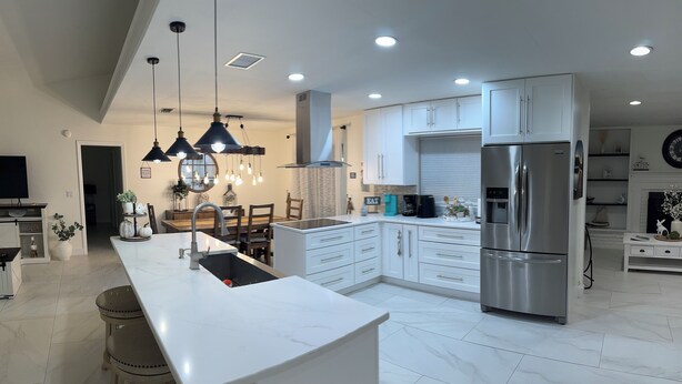 Une cuisine moderne avec des meubles blancs, des appareils en acier inoxydable et des luminaires suspendus.