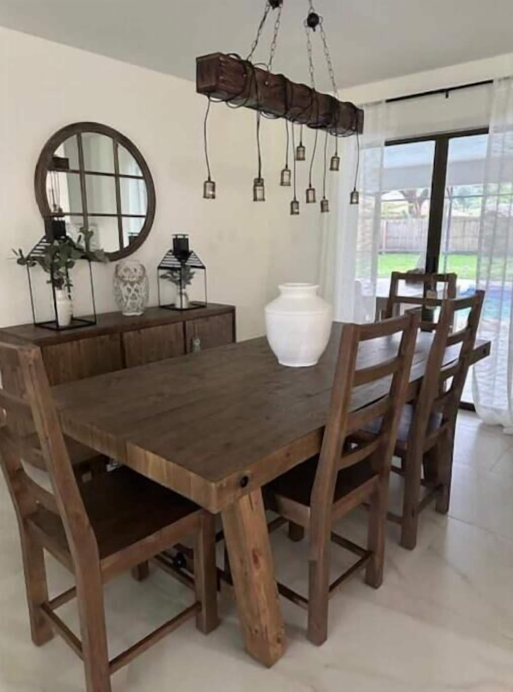 A dining area with a wooden table and chairs, a large mirror, and hanging pendant lights.
