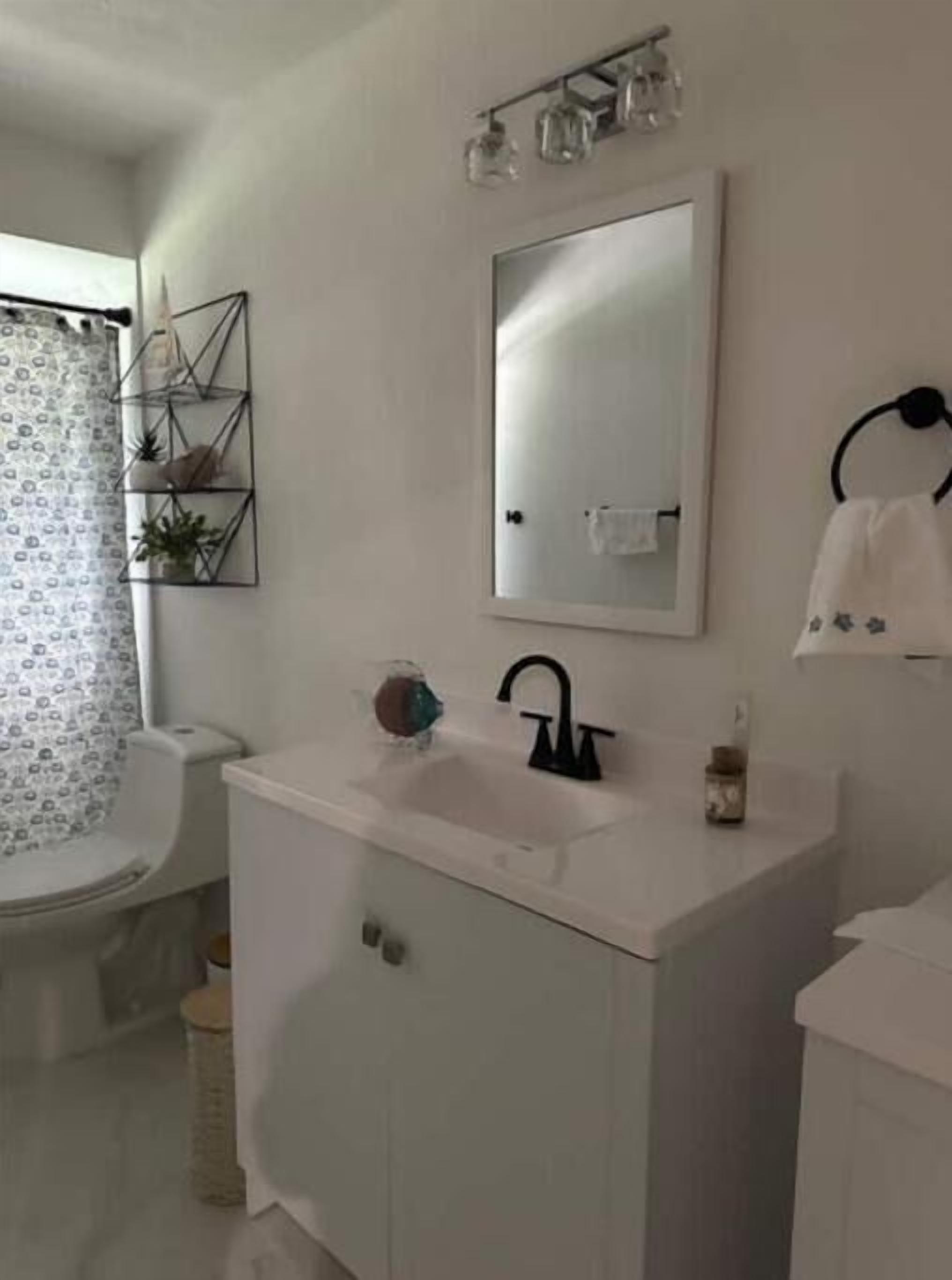 A bathroom with a white sink, a mirror, and a toilet. There is a towel rack on the wall and a small shelf with plants.