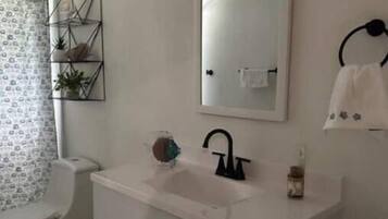 A bathroom with a white sink, a mirror, and a toilet. There is a towel rack on the wall and a small shelf with plants.