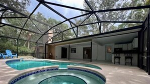 Une piscine extérieure couverte avec un fond en verre, entourée d’un patio agrémenté de chaises et offrant une vue sur les arbres.