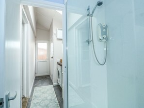 A narrow hallway leading to a bathroom with a shower, a washing machine, and a small window. - Windyridge (Skegness)