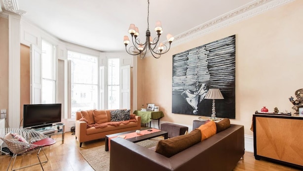 Ein modernes Wohnzimmer mit Sofa, Couchtisch und Fernseher. Es gibt ein großes Fenster und eine Deckenleuchte.