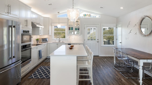 A modern kitchen with stainless steel appliances, a central island, and a dining area with a wooden table and chairs. - Dot's Spot, Almost Oceanfront House in Emerald Isle, NC! (Atlantic Beach)