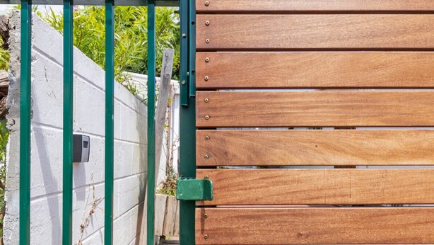 A wooden gate with a green metal frame and a white wall with a security device. - Peaceful 1BD Flat w/ Private Gardenrondebosch (Cape Town)