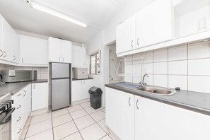 A modern kitchen with white cabinets, a stainless steel refrigerator, a microwave, and a sink. - Peaceful 1BD Flat w/ Private Gardenrondebosch (Cape Town)