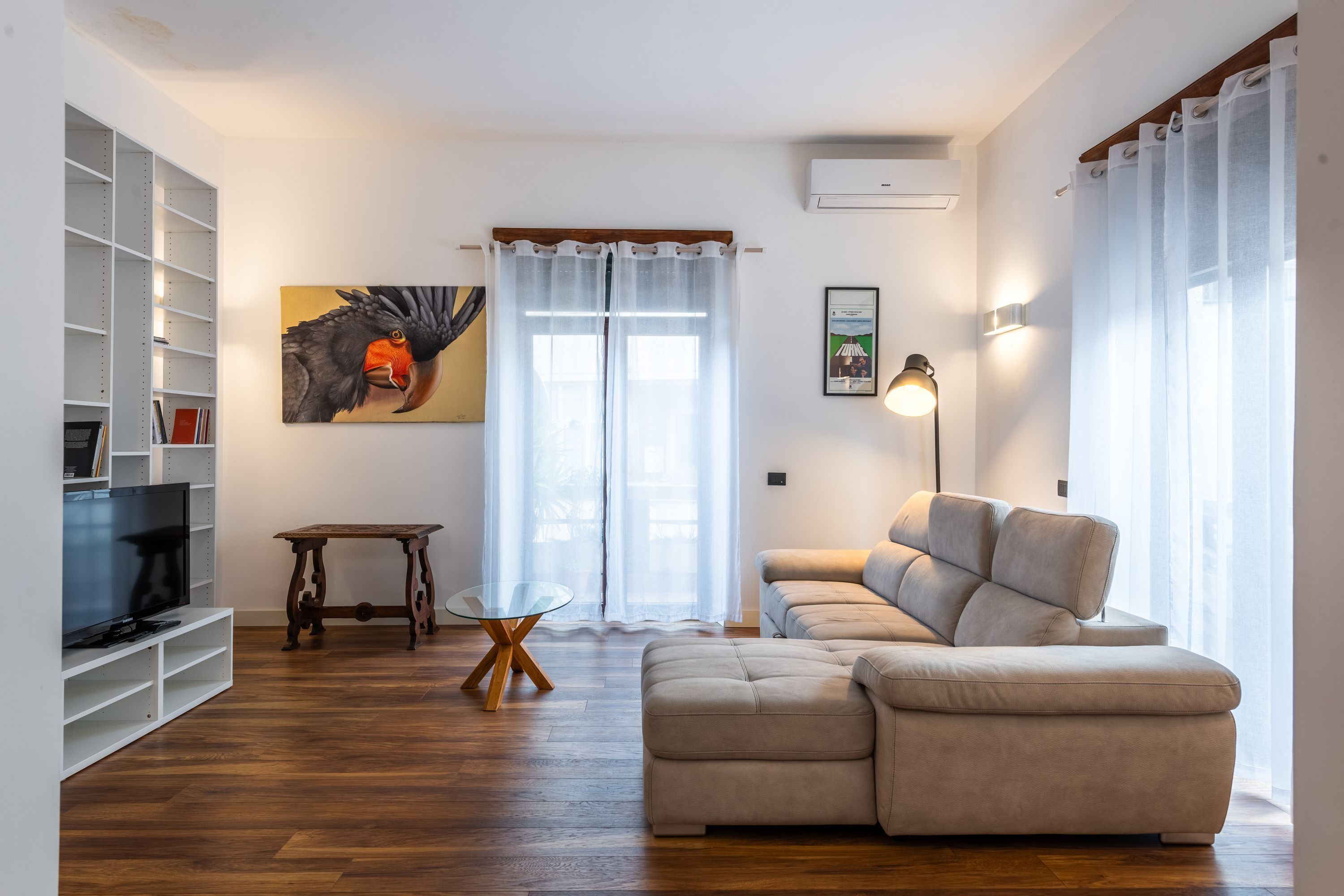Ein Wohnzimmer mit einer Couch, einem Fernseher, einem Glastisch und einem Gemälde.