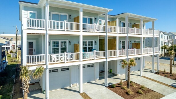 A multi-story residential building with balconies, a garage, and a landscaped front yard.